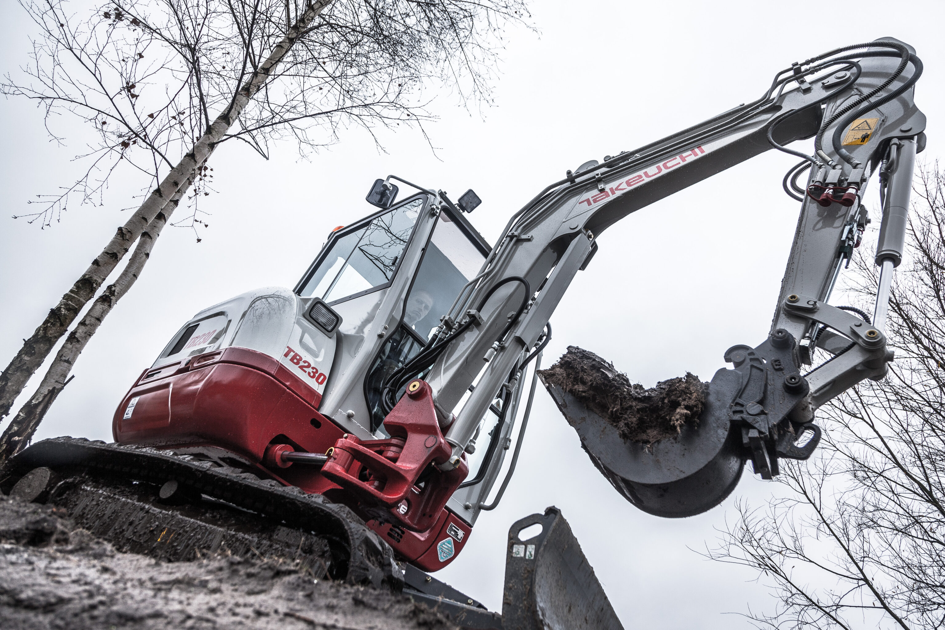 De Takeuchi TB230 minigraver vanaf beneden gefotografeerd met een banaanbak eraan