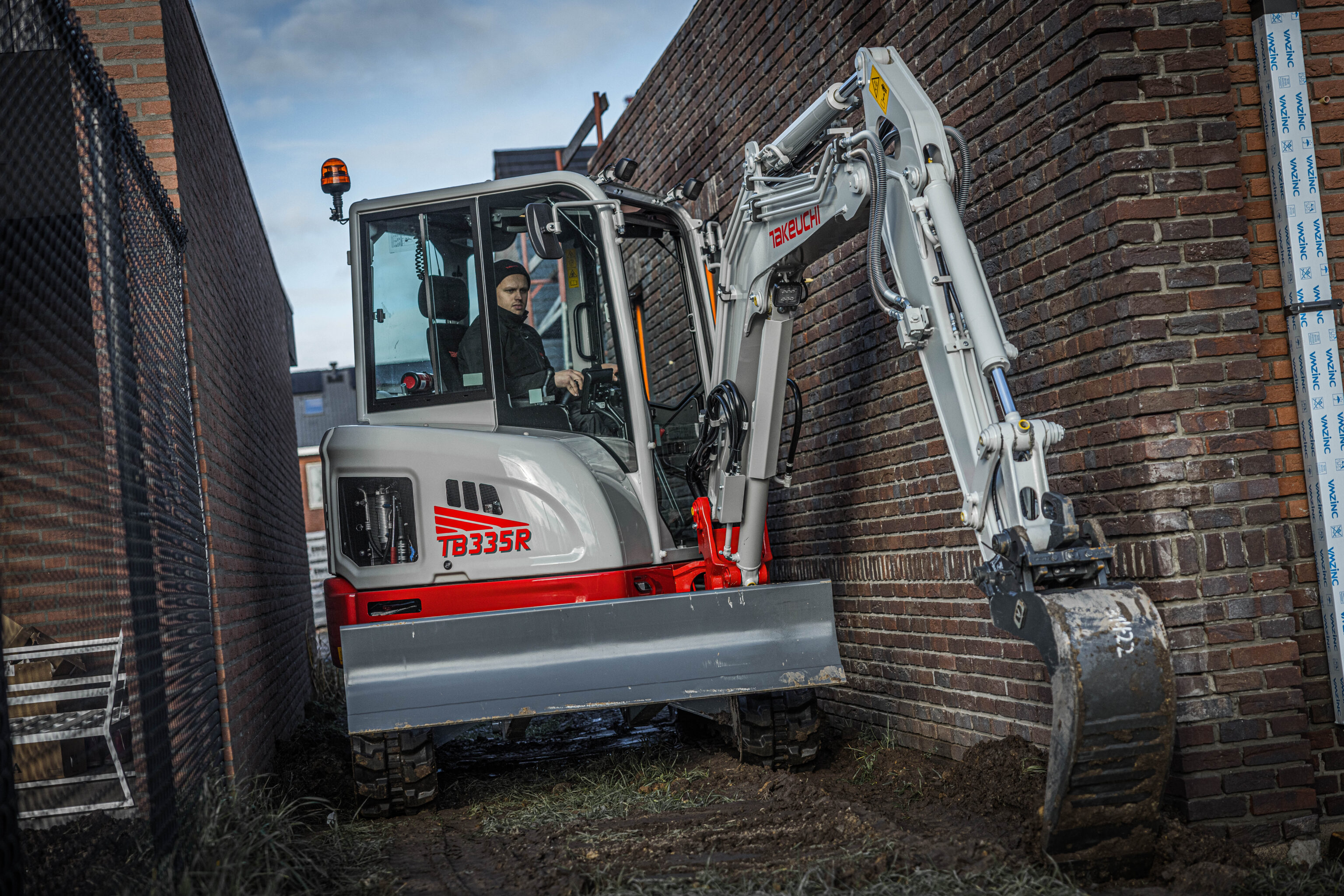 Takeuchi TB335R graafmachine rijdt door een smalle doorgang