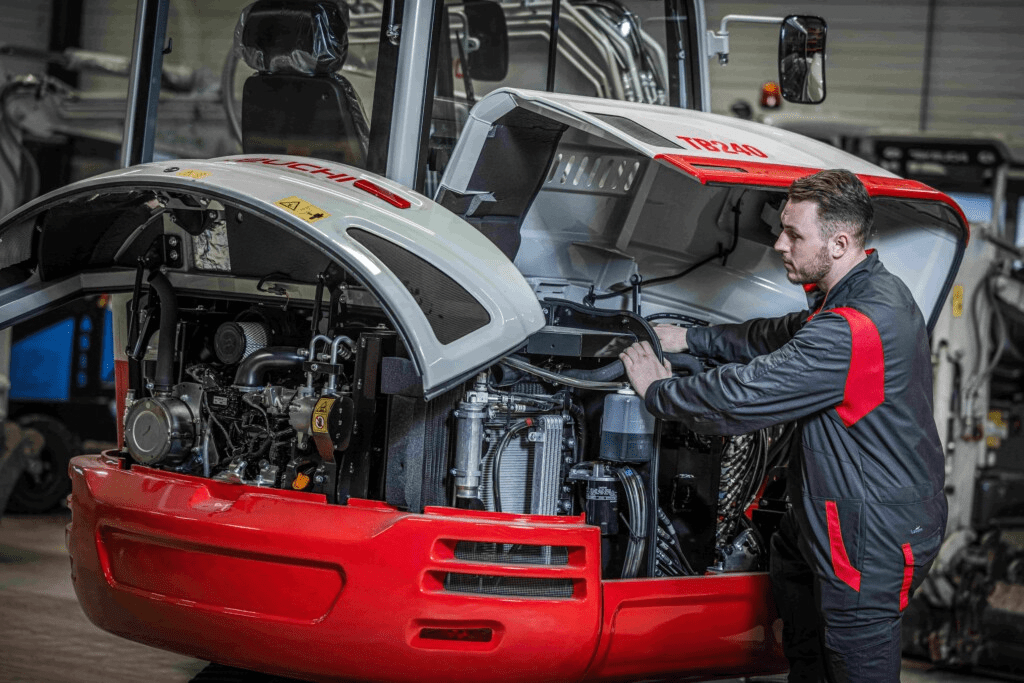 Takeuchi monteur bij graafmachine met motorkappen open