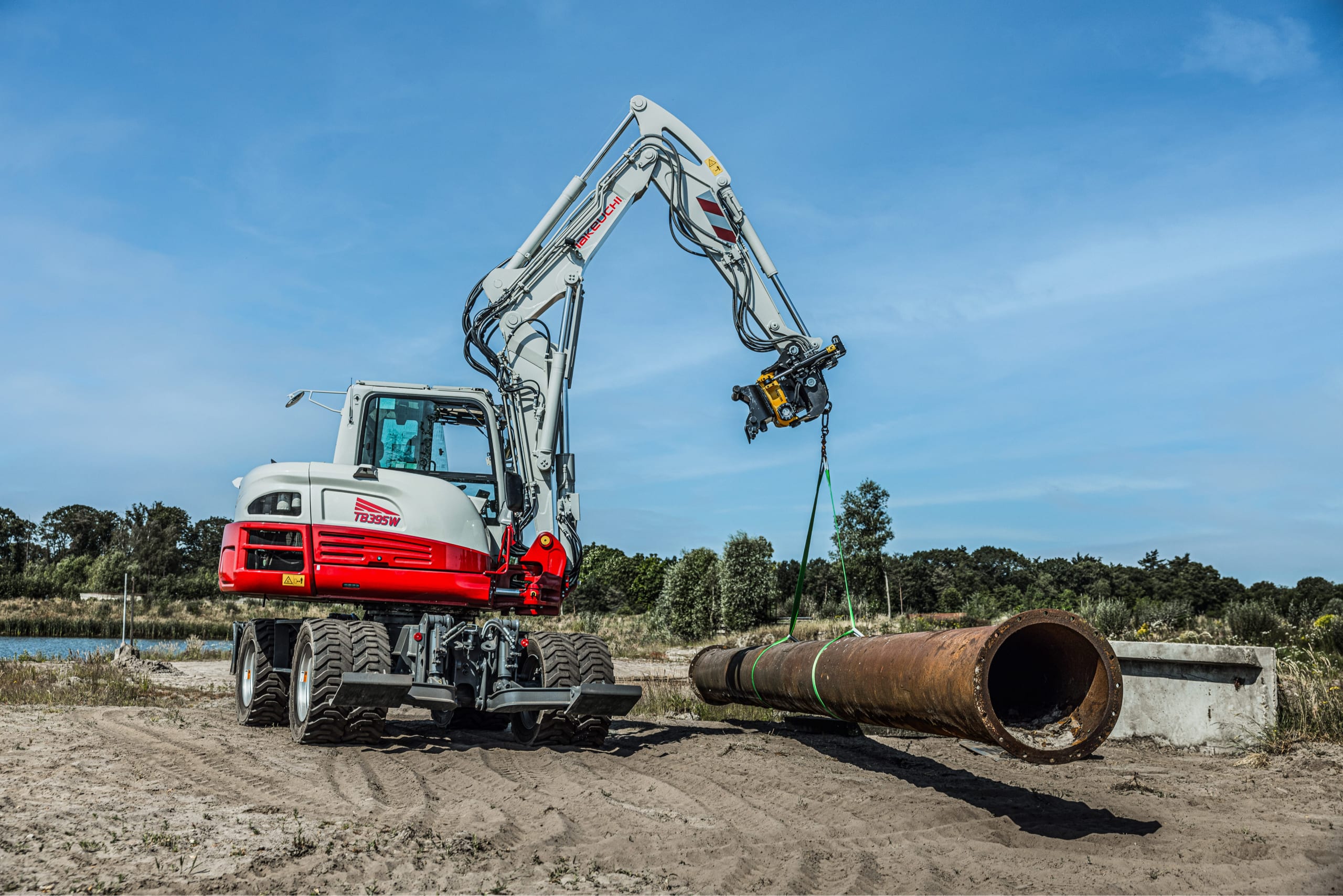 Een tb395w van Takeuchi die grote zware metalen buis ophijst om te verplaatsen