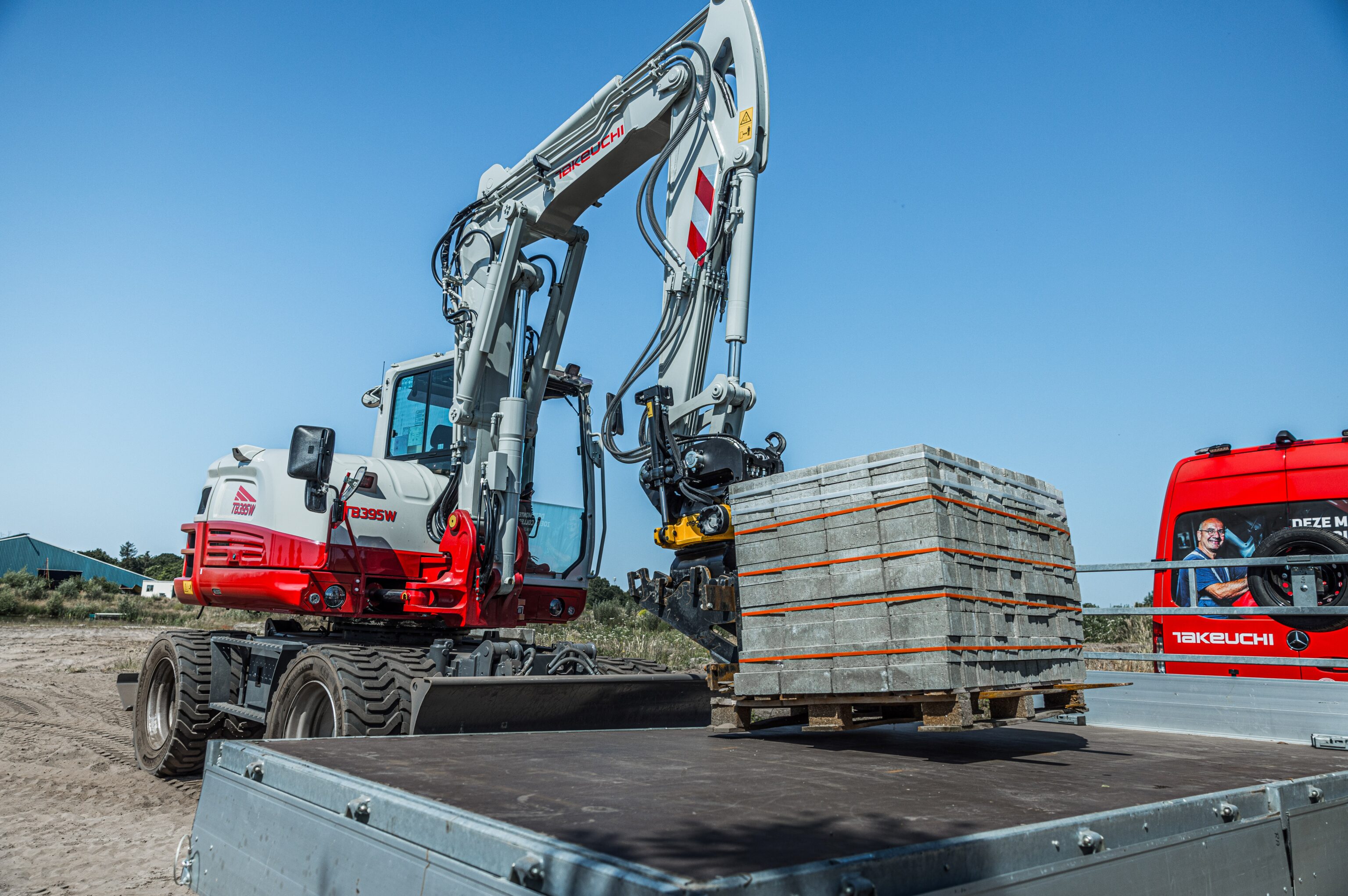 Takeuchi graafmachine tilt met een palletvork een volle pallet stenen van een aanhanger